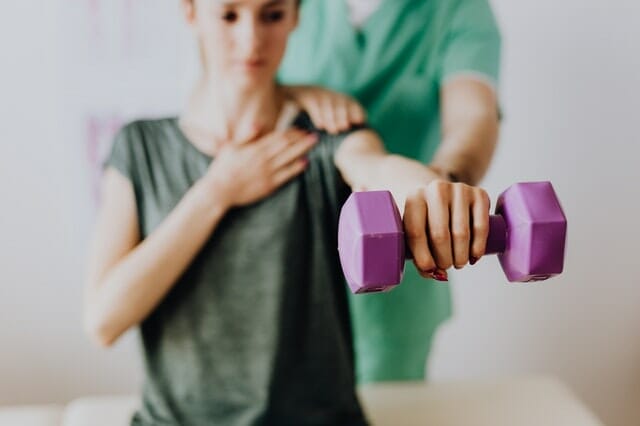 A chiropractor guiding his patient holding a dumbbell