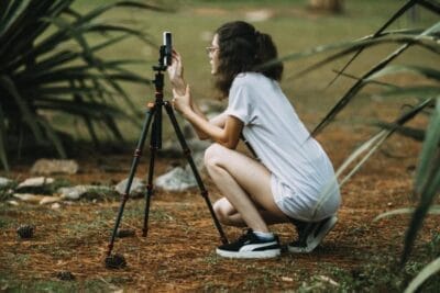 A Girl Crouching on the Ground Using Her Smartphone on a Tripod
